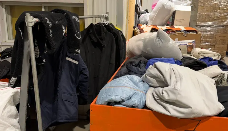 Coats on a rack and clothing being sorted in a large bin